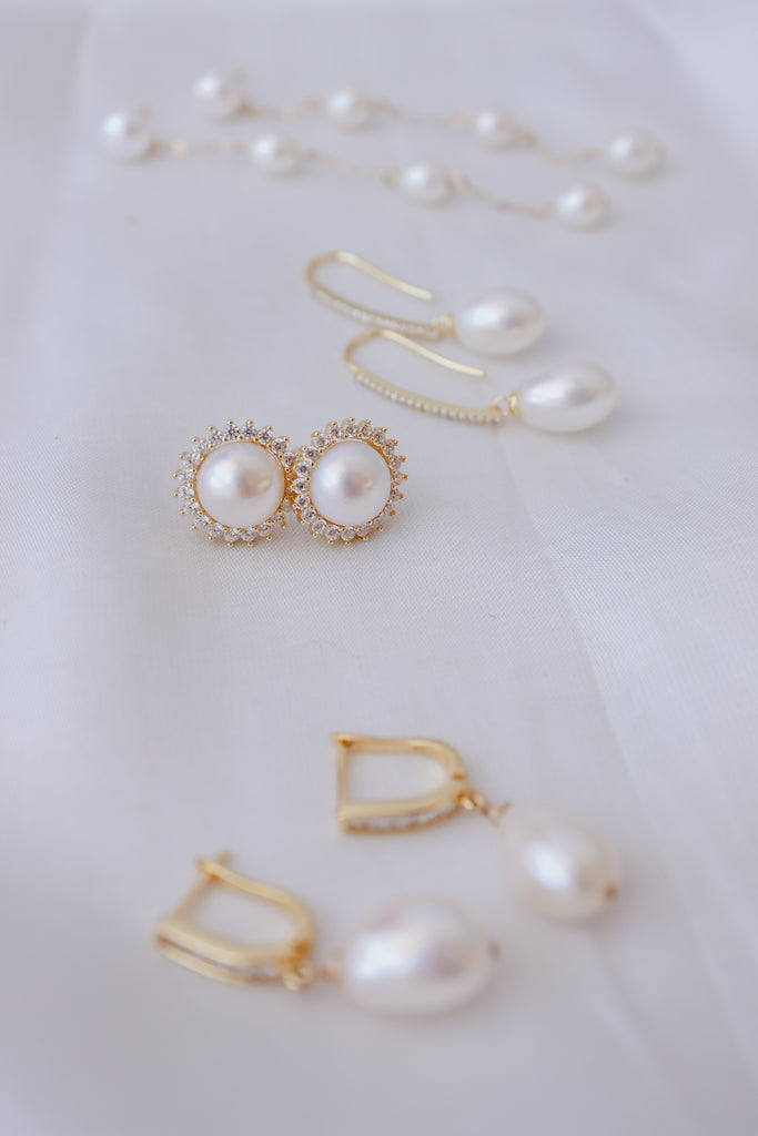 Various styles of pearl bridal earrings hanging on a gold jewellery stand